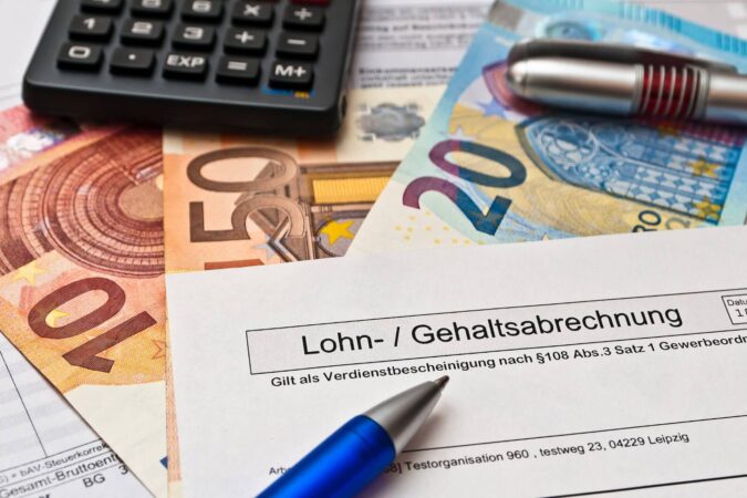 Auf einem 10, 20 und 50 Euroschein liegt ein Zettel, auf dem Lohn- und Gehaltsabrechnung steht.