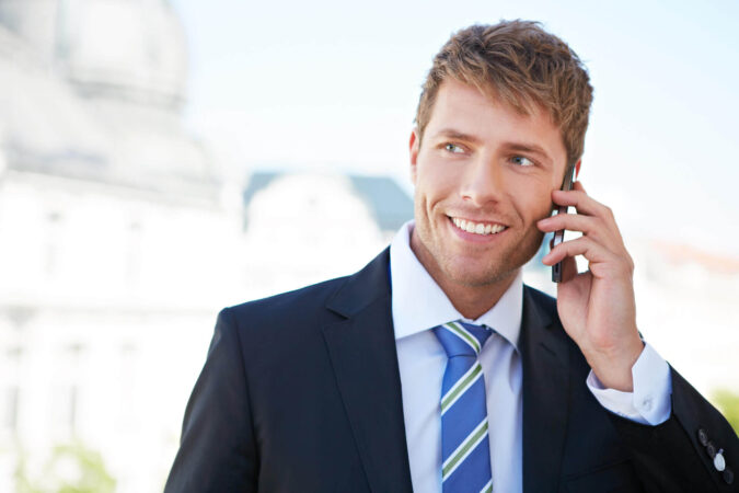 Ein Mann im Anzug hält lächelnd ein Handy an sein Ohr und telefoniert.